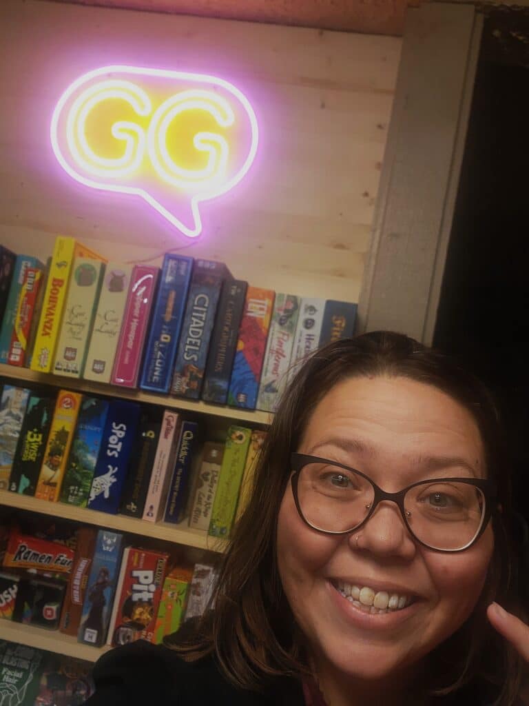 Board Game Enthusiast in front of a GG Neon sign and board game shelf